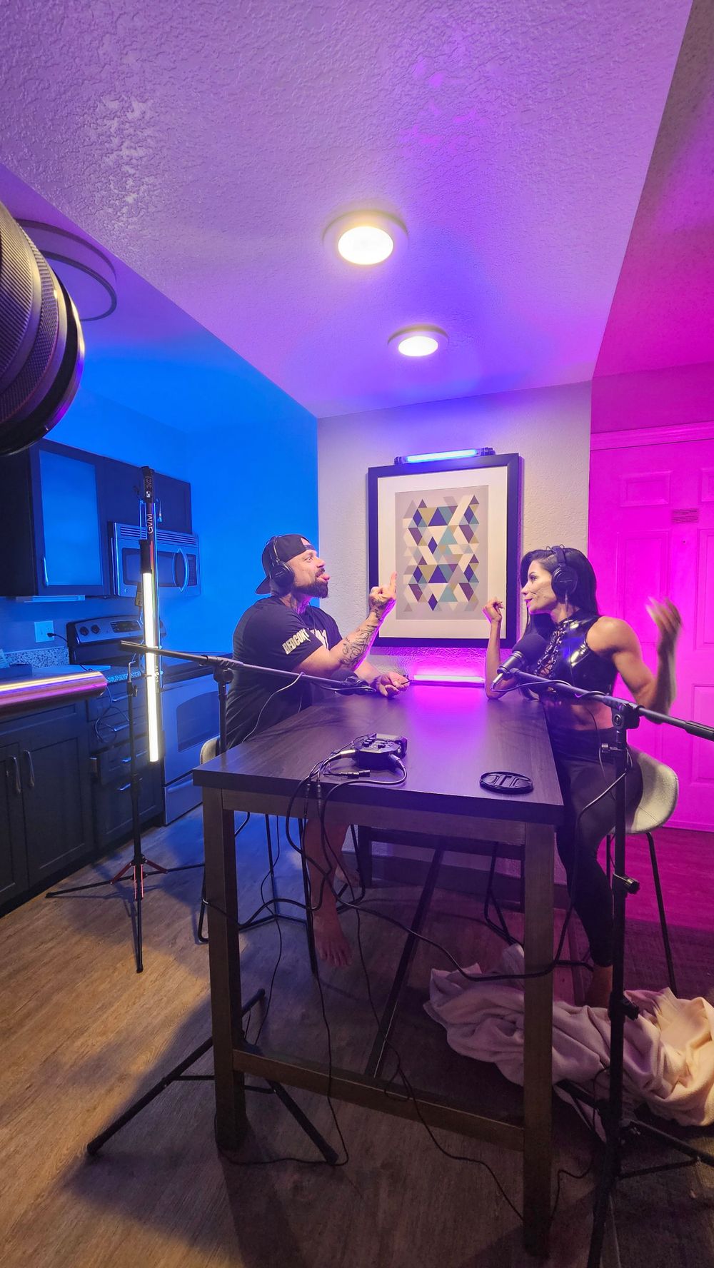 Two people recording a podcast in a room with colorful LED lighting and professional microphone setup.