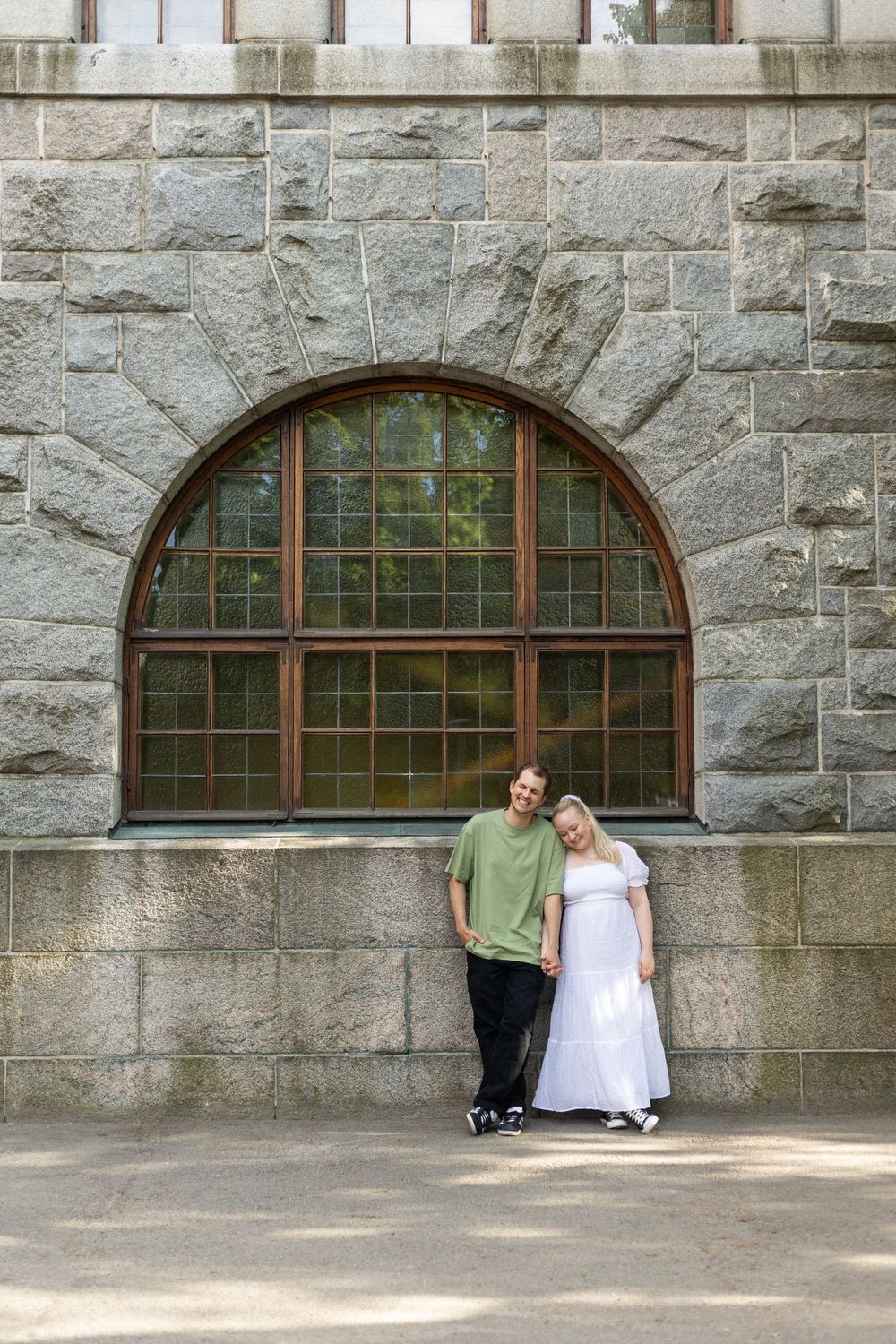 Casual wedding portrait against stone wall with arched window architecture.