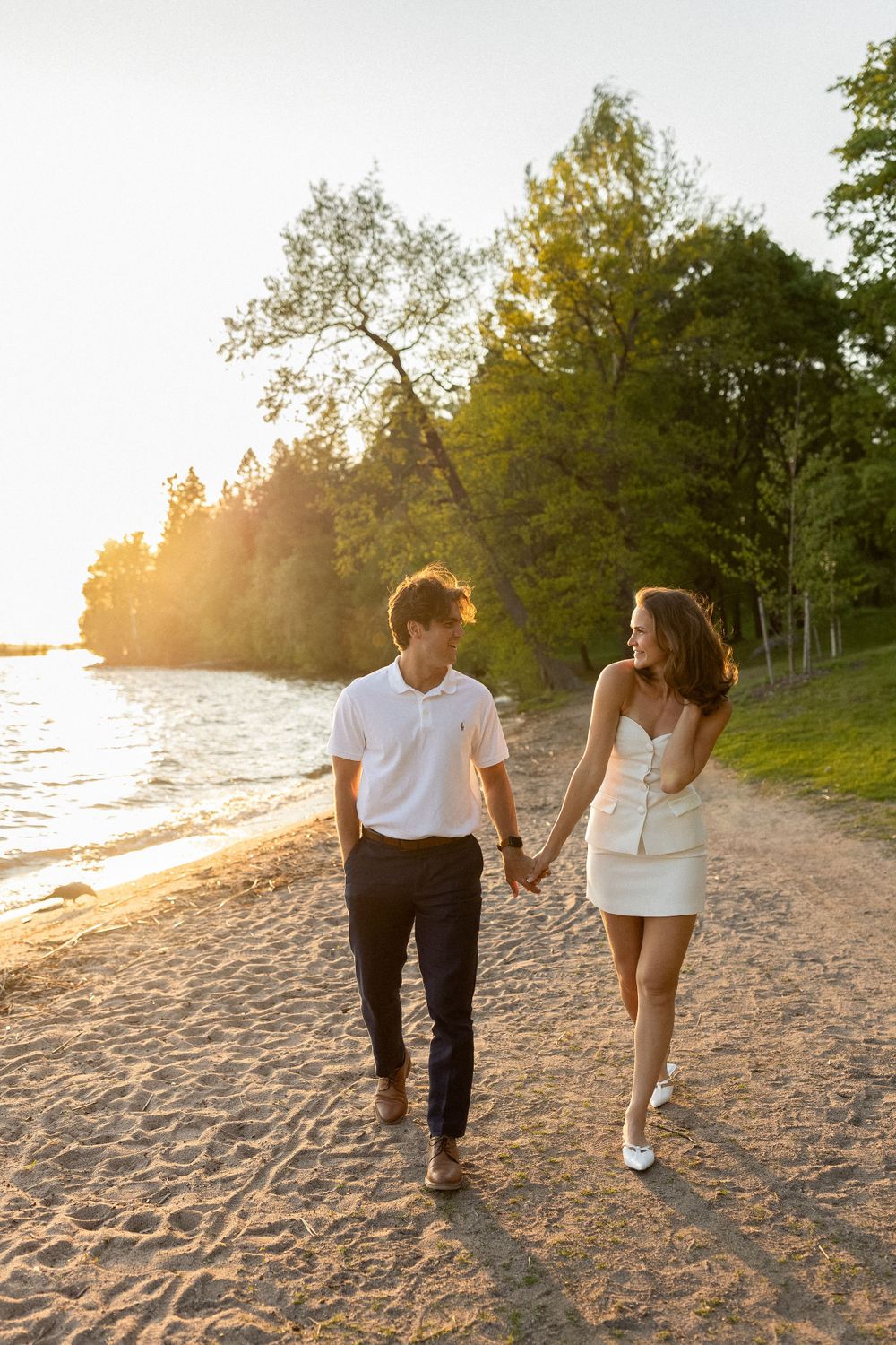 Couple walking hand in hand along a sandy beach at golden hour.