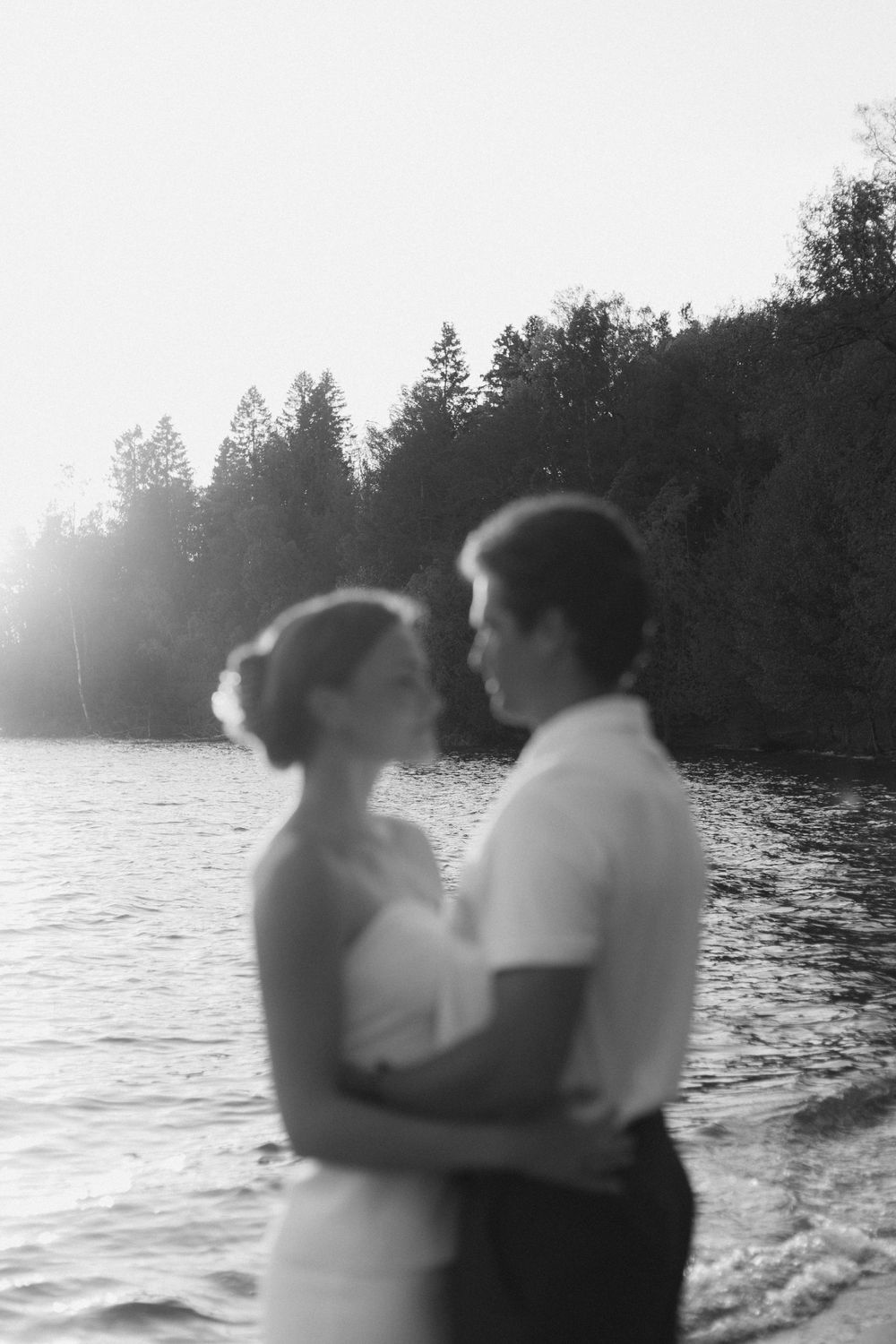 Black and white silhouette of couple embracing by waterfront at sunset.