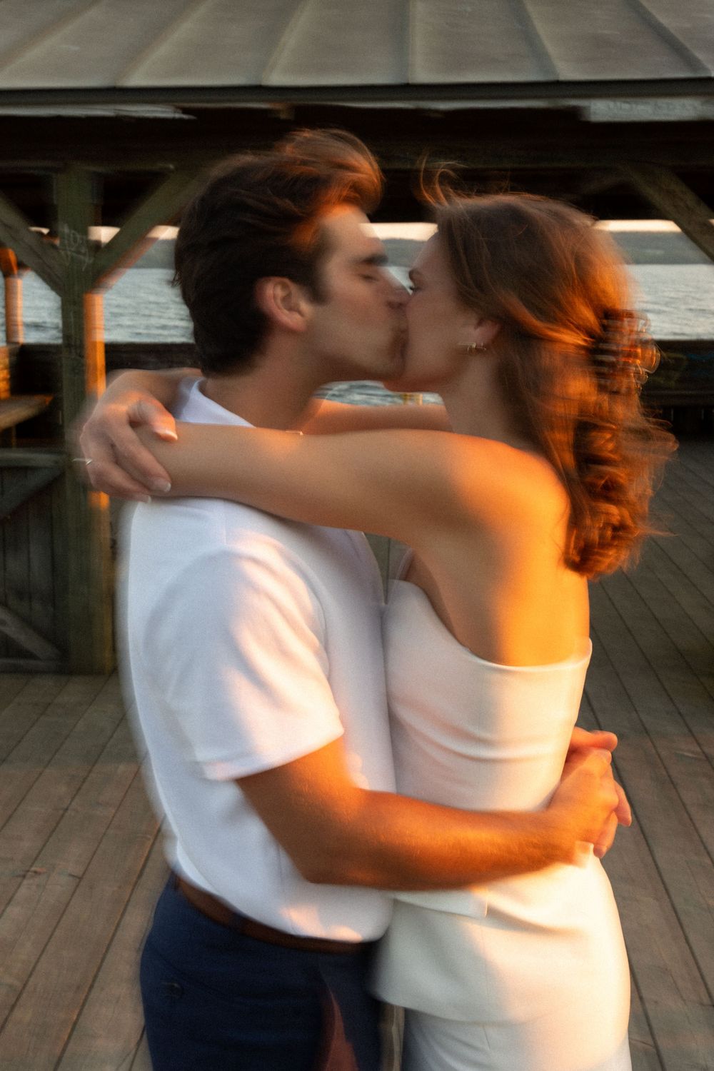 Intimate sunset kiss on wooden deck with warm golden light.