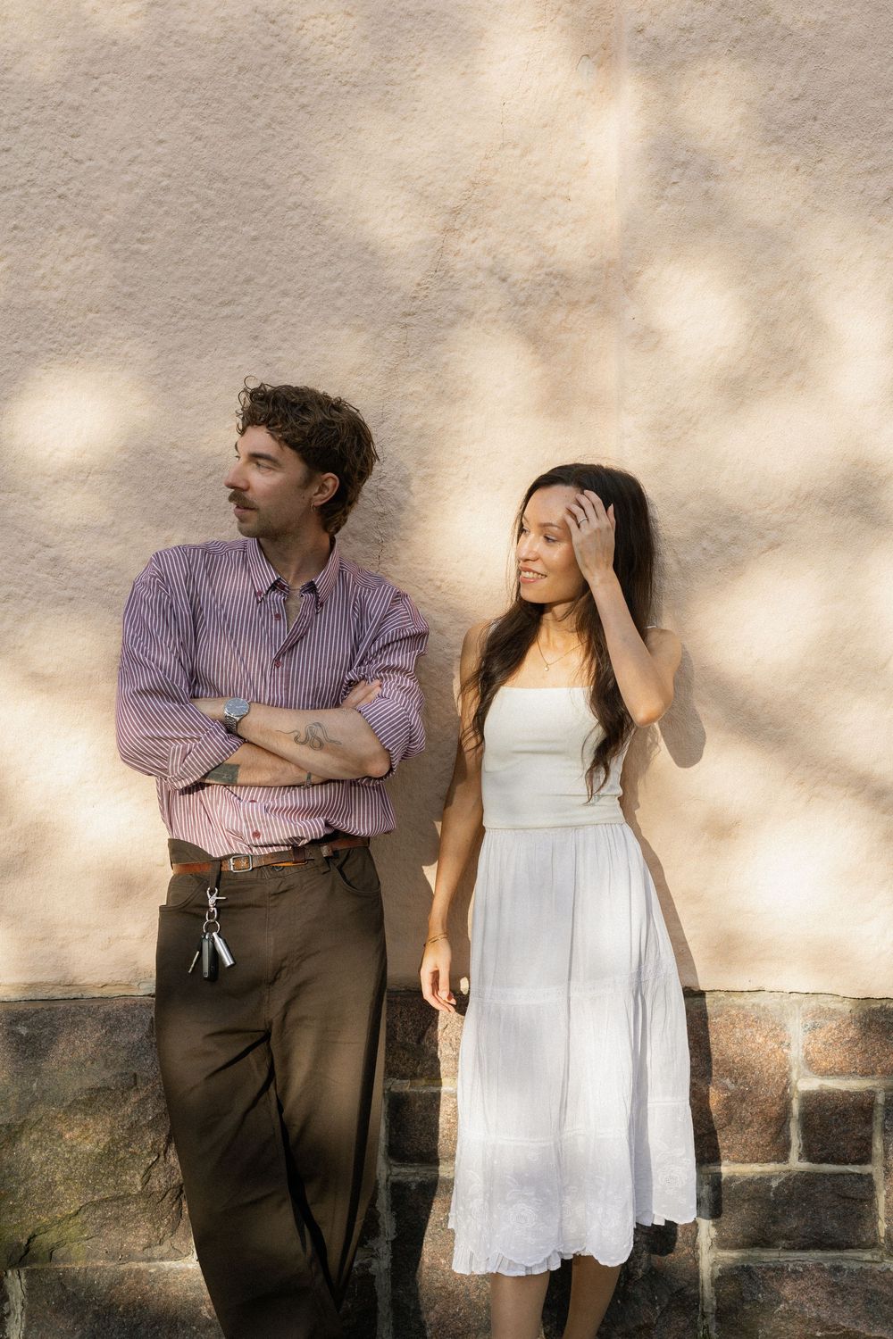 A couple interacting with expressive body language against a light colored wall in an outdoor setting.