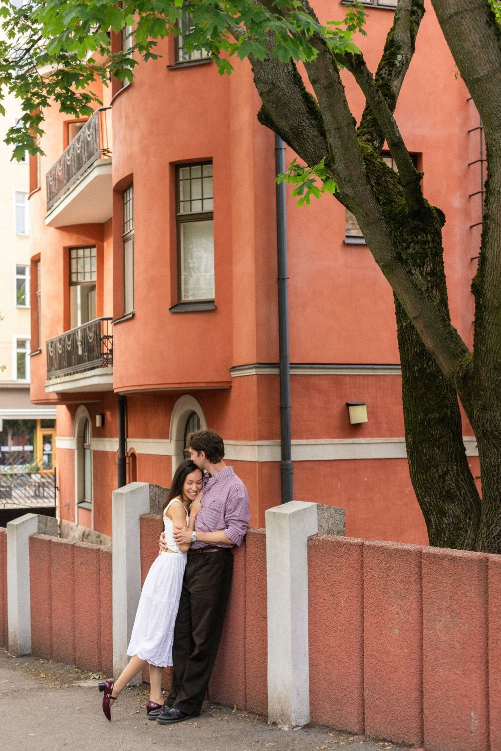 A series of romantic moments captured against a coral-colored building wall with green trees overhead.