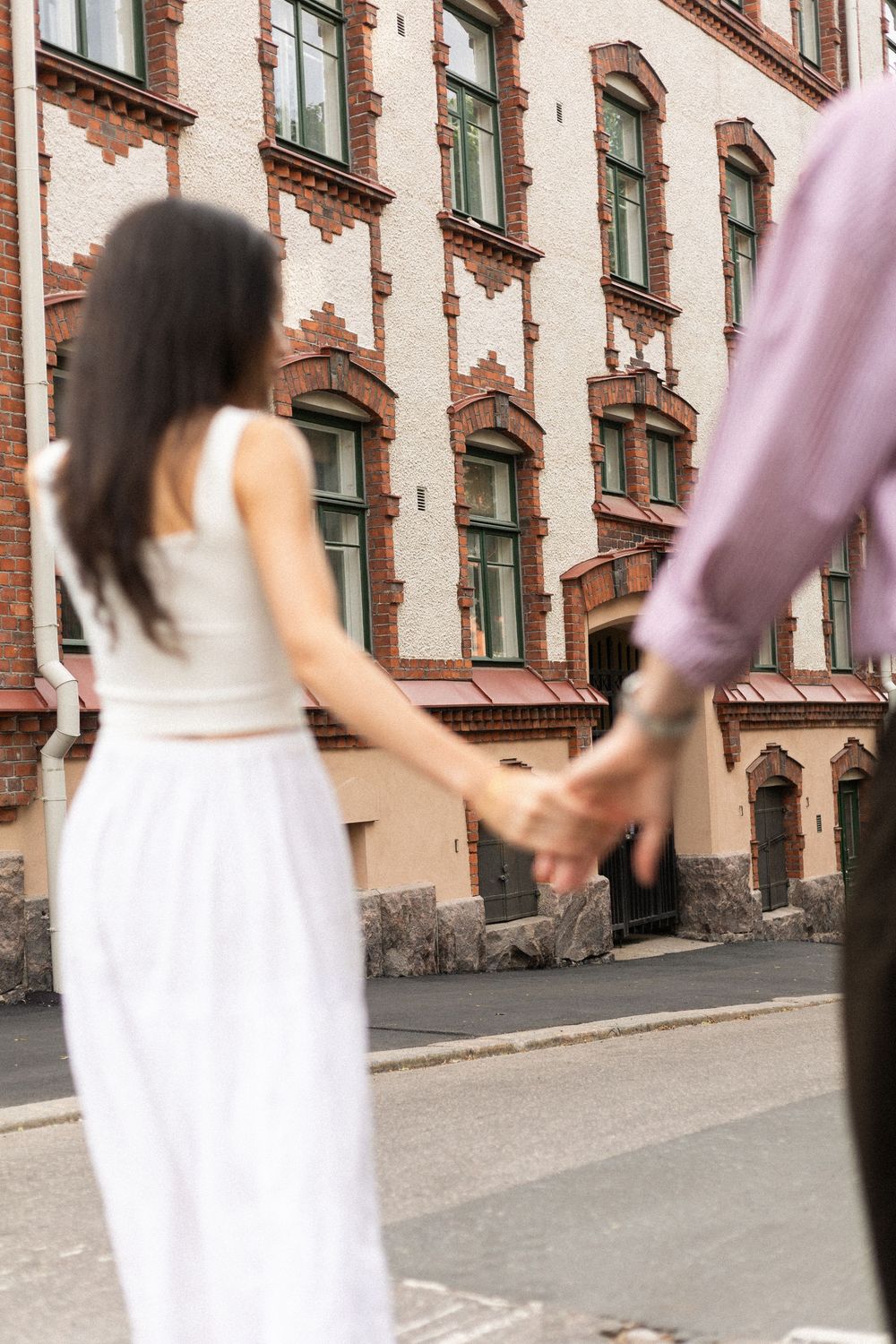 Motion-blurred sequence of a person in a white dress walking past a historic brick building with green windows.