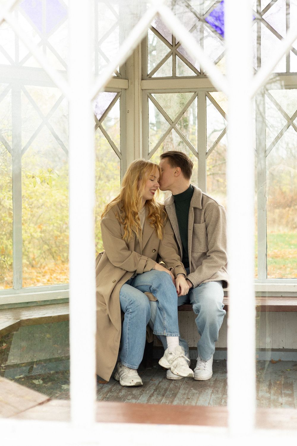 A romantic couple sits close together on a covered porch bench during autumn.