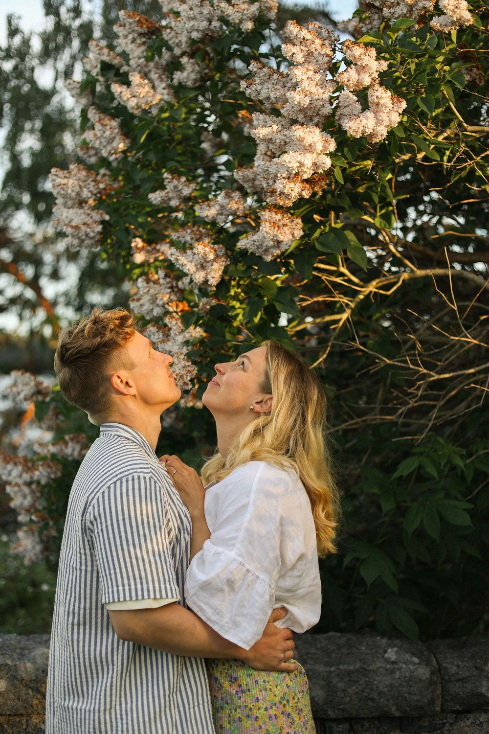 Romantic couple embraces beneath blooming cherry blossoms in a spring garden setting.