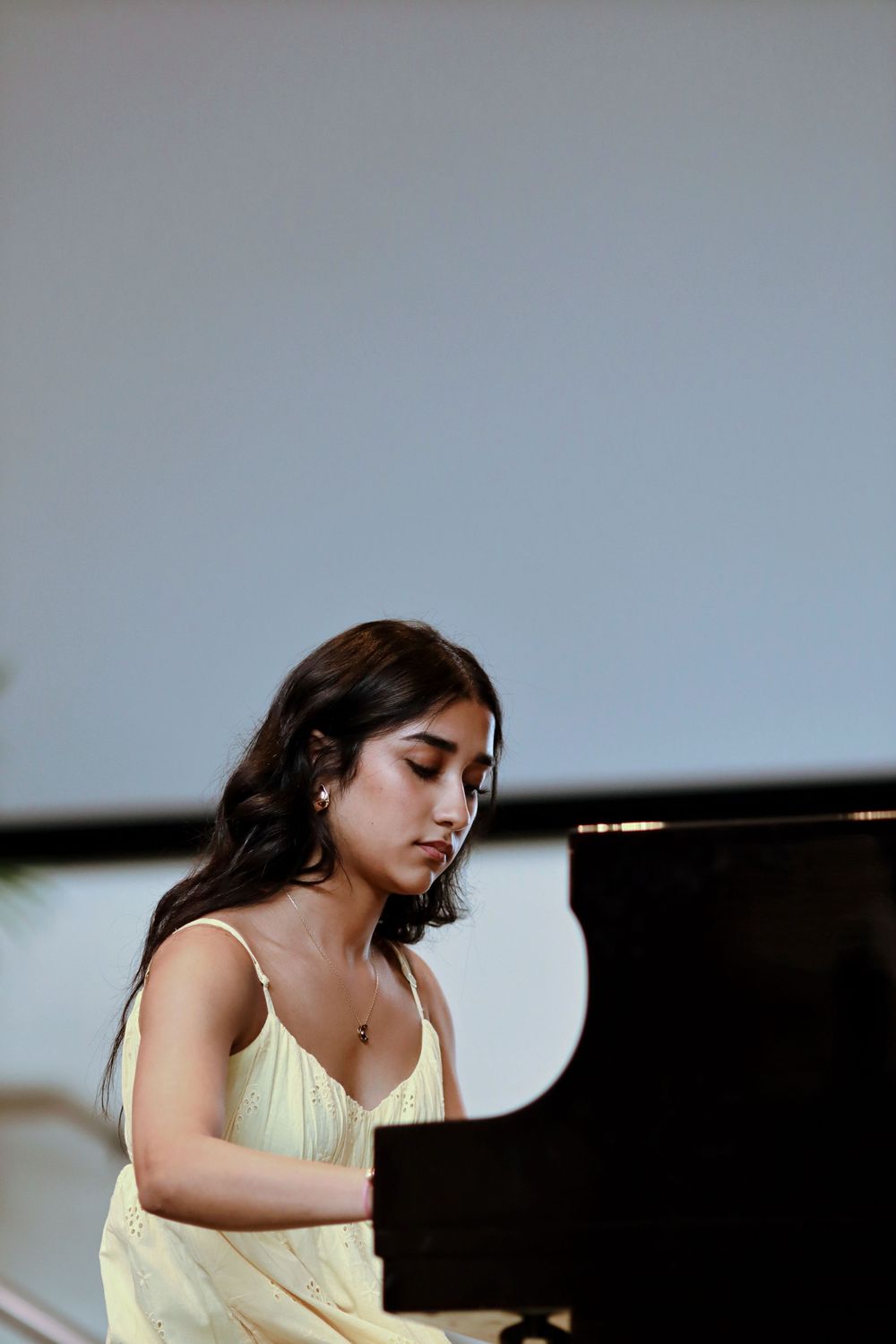 Young woman in yellow dress playing grand piano, focused expression, performing at a recital.