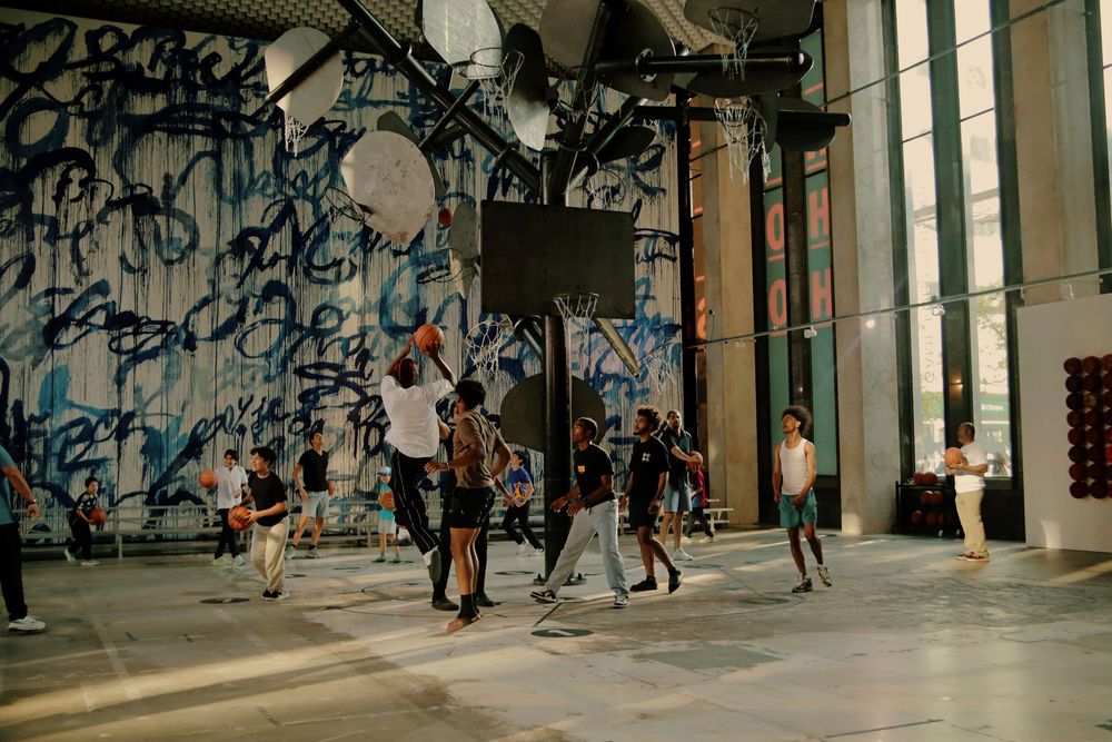 Basketball players compete in a street court with graffiti-covered walls in an urban setting.