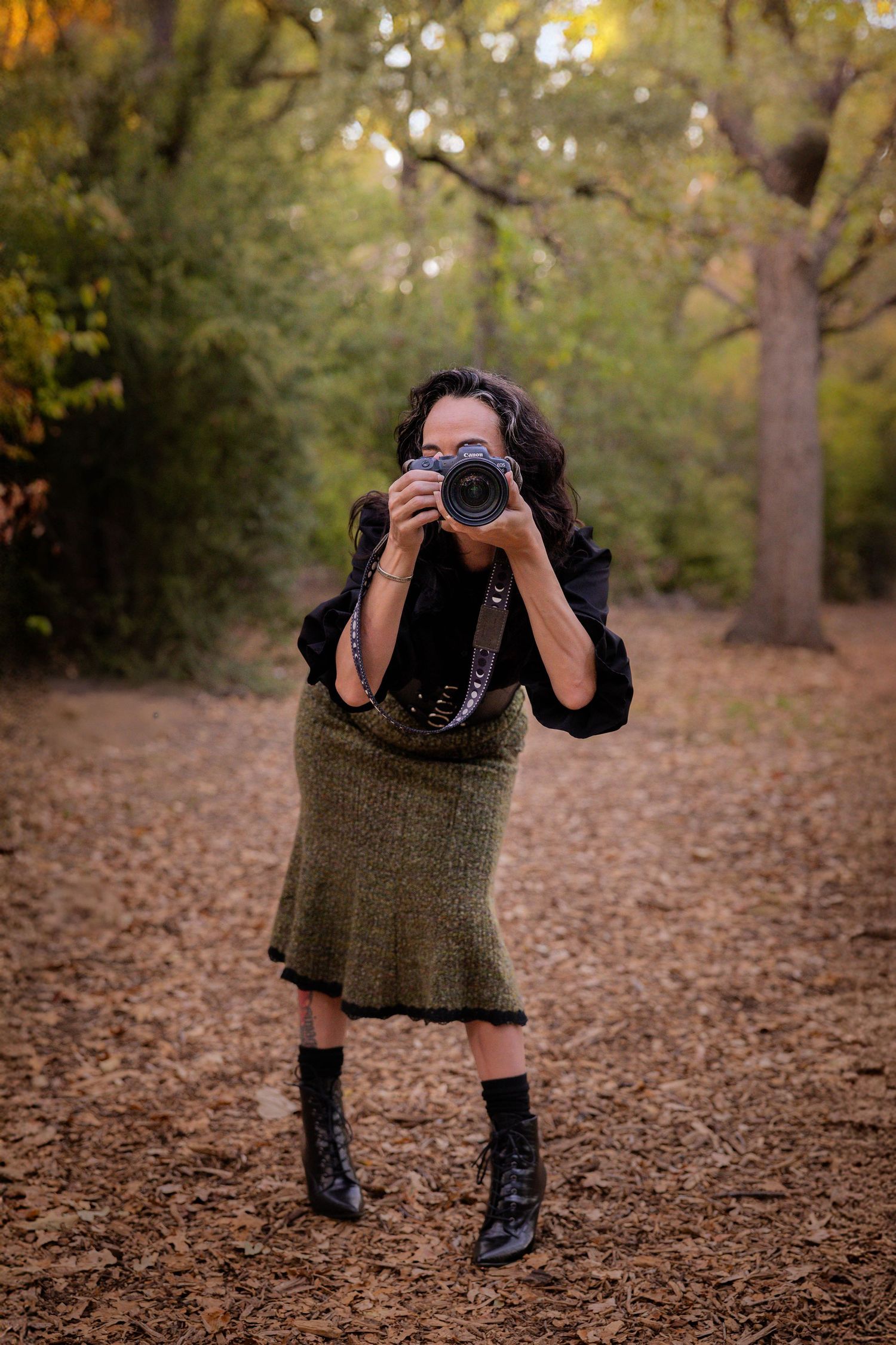 A woman poses with her camera pointed at the camera.