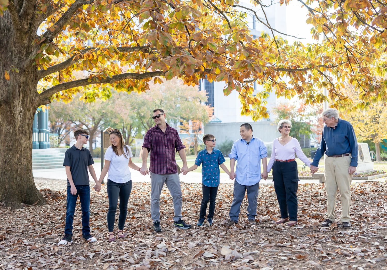 A family portrait together under a large autumn tree with golden leaves as fallen foliage covers the ground below in Marietta, Georgia.