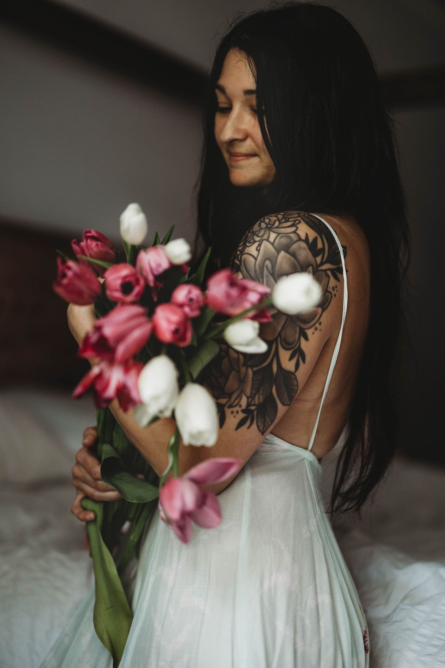 Young woman with long dark hair, gazing at tulips in arms while wearing long dress