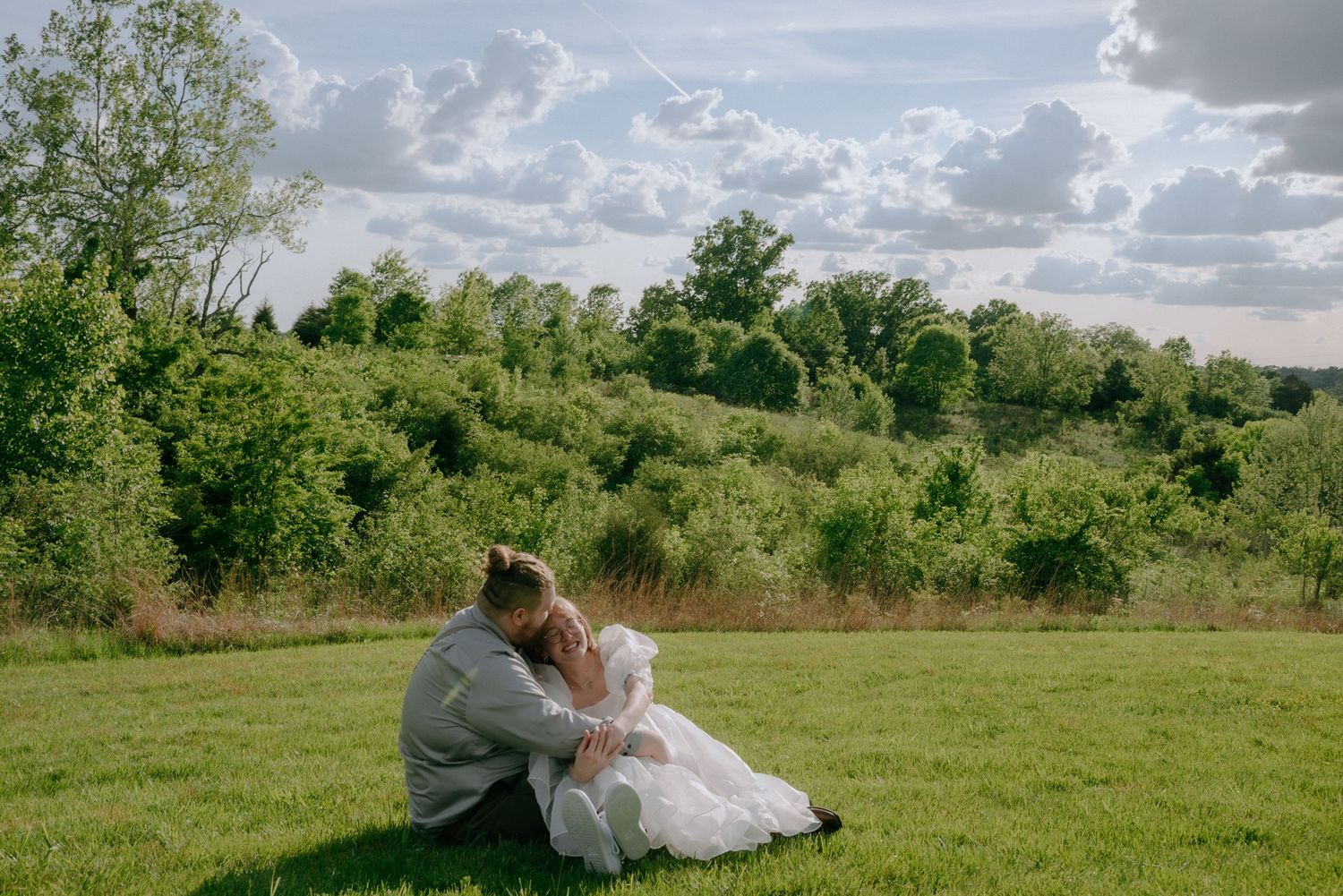Scenic panorama of a green meadow with dramatic clouds and rolling hills in the background during wedding photoshoot.