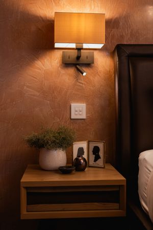 Warm-toned bedside table with modern wall sconce, decorative plant, and framed artwork. Interior design photography in Surrey and Hants.