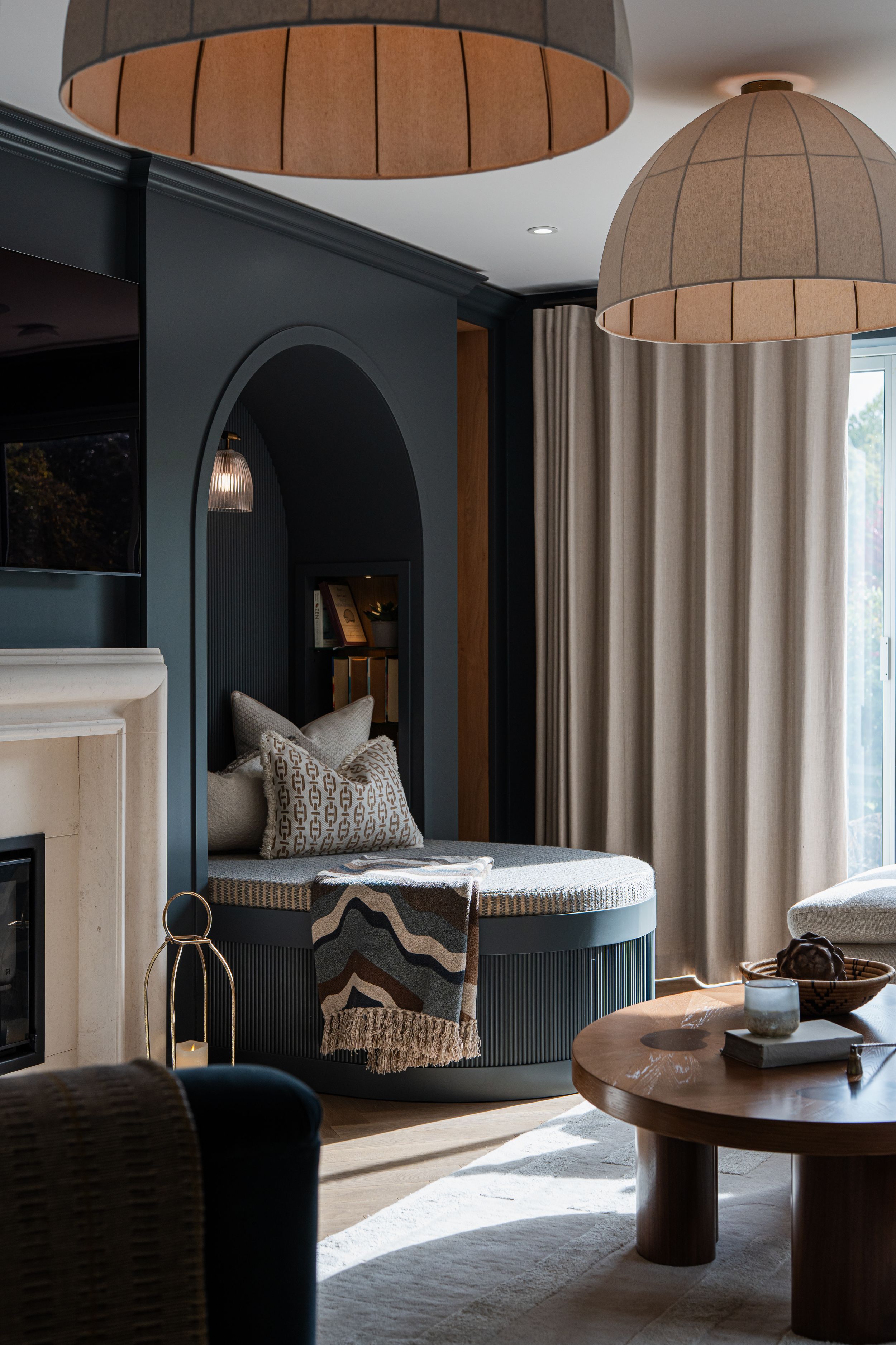Modern living room with dark walls featuring a cozy reading nook with curved archway and oversized dome pendant lights.