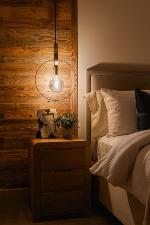 Modern bedside table with hanging pendant light against wood paneled wall. Interior design photography in Surrey and Hants.
