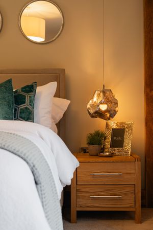Contemporary bedroom corner with geometric pendant light and circular mirror above wooden nightstand. Interior design photography in Surrey.