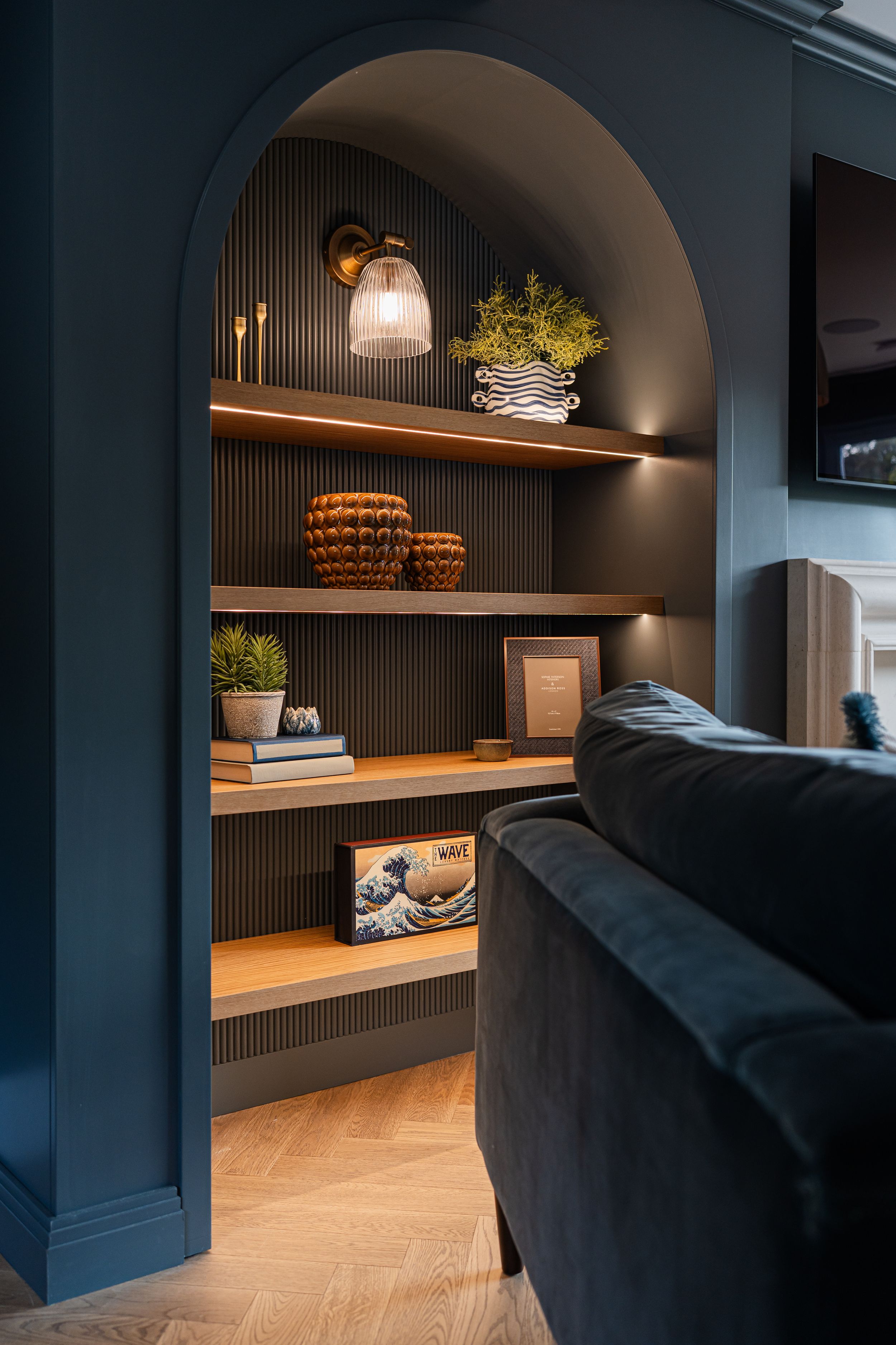 Modern bedroom nook features dark walls, floating wooden shelves, and black bedding with ambient lighting.