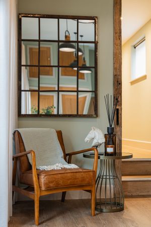 Cozy reading nook with mid-century modern chair and industrial window mirror in natural light. Interior design photography in Surrey.