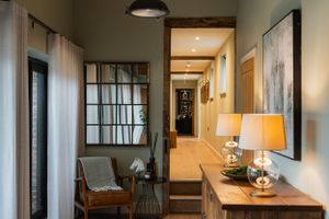 Stylish corridor with window-pane mirror, accent chair, and warm lighting leading to hallway. Interior design photography in Surrey.