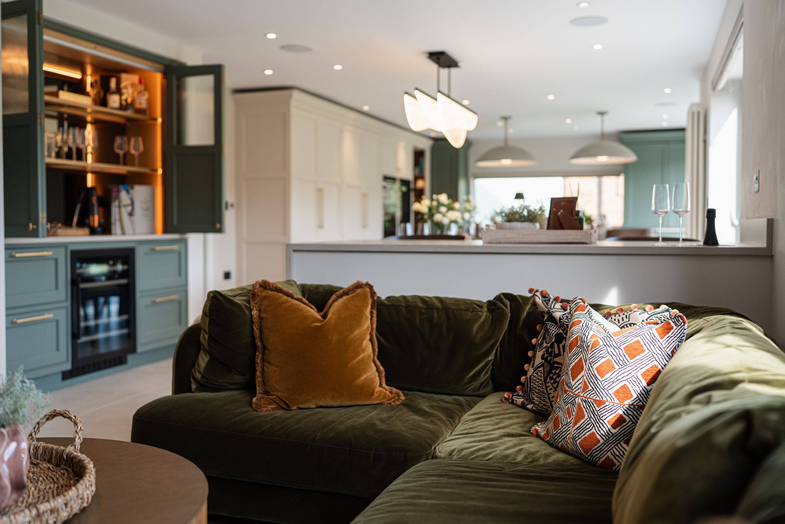 Modern basement living room features dark sectional sofa, colorful throw pillows, and recessed lighting in warm tones.