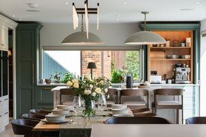 Contemporary kitchen features dark green cabinetry, white countertops, and pendant lighting over a wooden dining table.