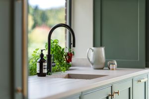 Modern white kitchen interior with sage green cabinets, quartz countertops and stainless steel appliances.