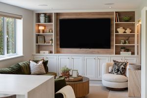 Bright living room with built-in white cabinets, mounted TV, and comfortable seating arrangement near large windows.