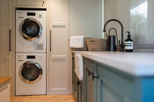 Modern laundry room with stacked white washer and dryer units, blue cabinets, and matte black faucet on quartz countertop.