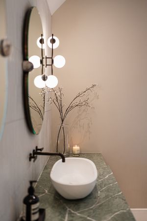 Modern white vase with dried branches sits atop marble surface under contemporary pendant lighting.