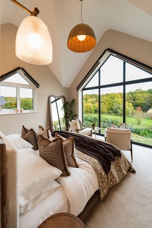 Luxurious bedroom with vaulted ceiling, panoramic windows and pendant lighting overlooking scenic countryside views.