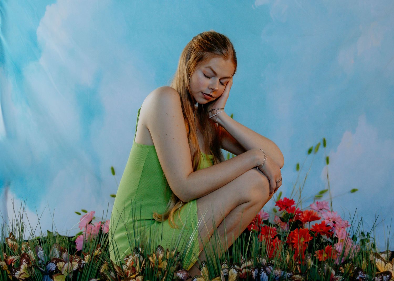 A woman in a green dress reclines peacefully among vibrant red poppies and wildflowers in a summer meadow.