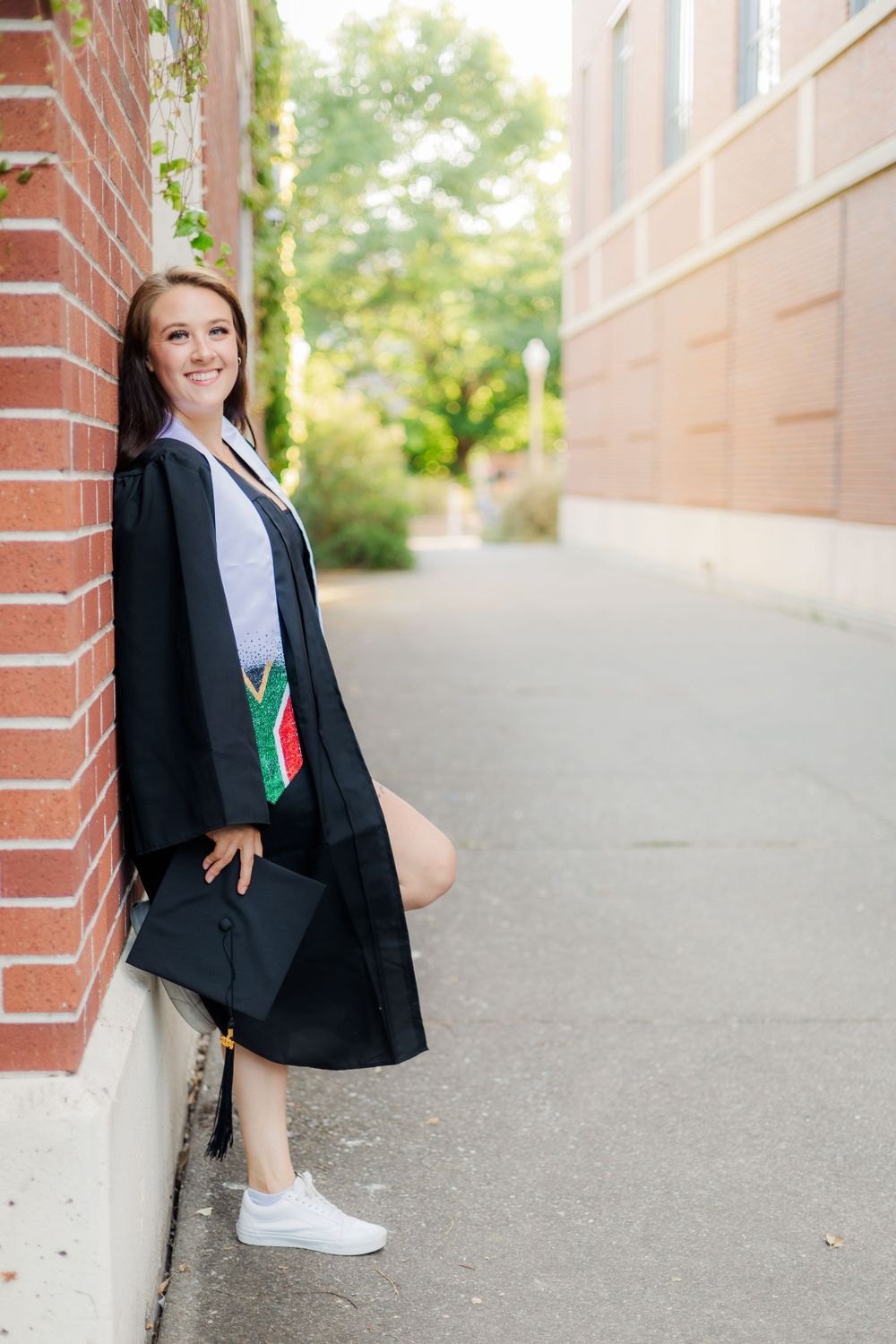 college senior leaning against brick wall for graduation photos in Santa Rosa, Sonoma County, California. cap and gown.