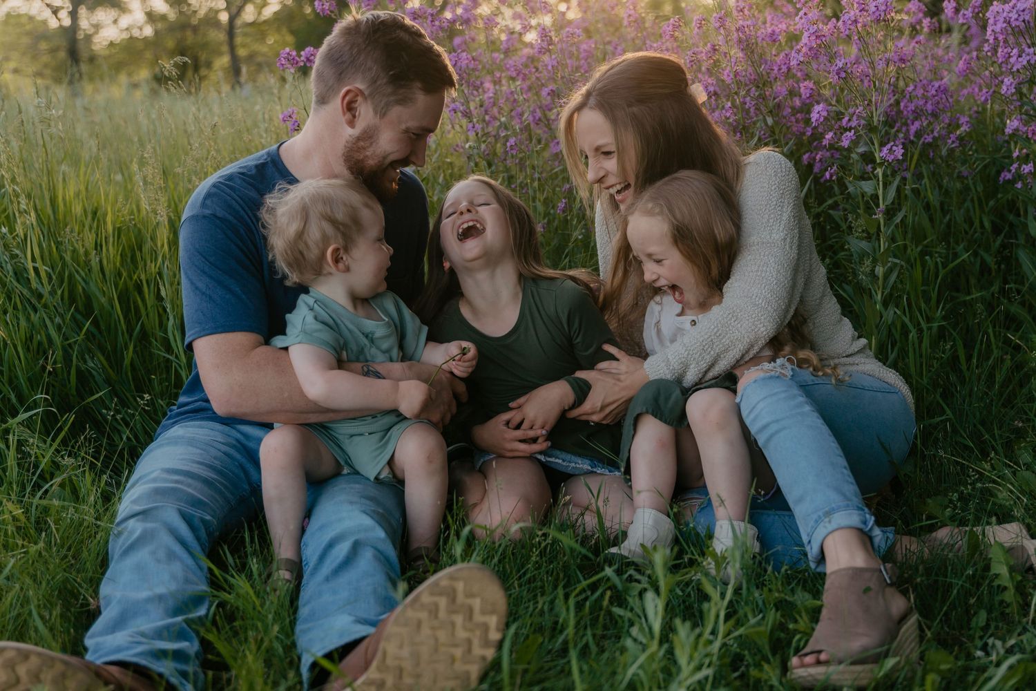 A family shares a joyful moment together while sitting in a field of purple wildflowers at sunset.
