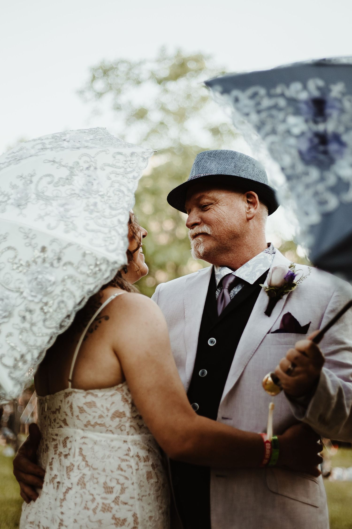 A tender wedding moment captured outdoors with an umbrella visible in soft light.