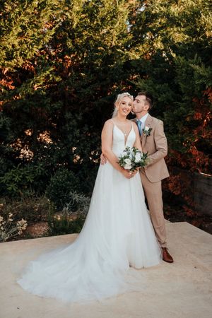 A romantic wedding couple shares an intimate moment on a stone ledge during golden hour sunset.
