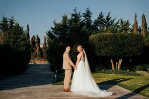 Wedding couple poses together in a scenic outdoor garden setting with evergreen trees in the background.