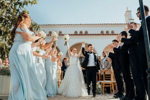 Wedding party celebrates with joy during outdoor ceremony at venue with white Spanish-style architecture.