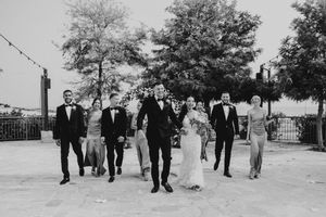 A black and white wedding party walks together outdoors on a sunny day with trees in the background.