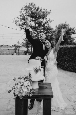 A joyful wedding couple poses playfully in a series of four black and white photos outdoors near a stone wall.
