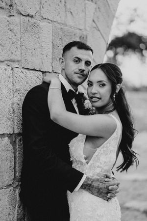 Black and white wedding photos show romantic moments between newlyweds against a stone wall backdrop.