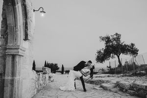Black and white panoramic photograph of a Mediterranean coastal landscape with stone buildings and cypress trees.