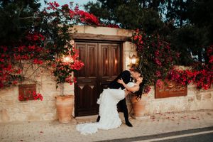 Red bougainvillea flowers cascade over a rustic stone wall with wooden doors creating a romantic Mediterranean scene.