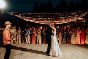An outdoor evening wedding reception with string lights overhead as guests gather to watch a dance.