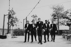 A black and white photograph shows a group of people in formal attire walking together on an outdoor terrace.