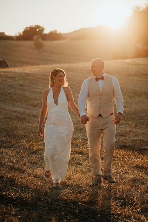 A couple walks hand in hand through a golden field at sunset, creating silhouettes against the warm glowing sky.