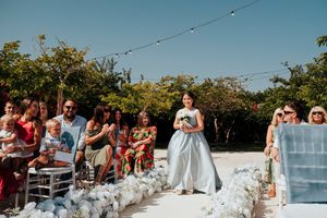 A panoramic view of a wedding ceremony setup with white chairs and floral arrangements under a bright blue sky.