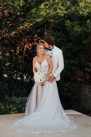 Romantic outdoor wedding portrait of couple embracing in a garden setting with lush greenery and flowing white gown.