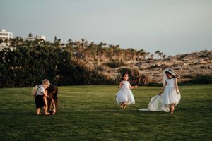 Wedding party enjoying a playful moment on a grassy lawn with palm trees in the background at sunset.