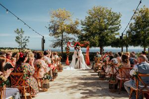 Wedding ceremony guests seated in white chairs on a sunny outdoor patio overlooking a scenic waterfront view.