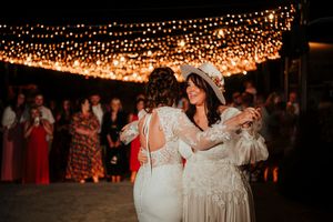 Wedding reception guests dance under romantic string lights at an outdoor evening celebration.